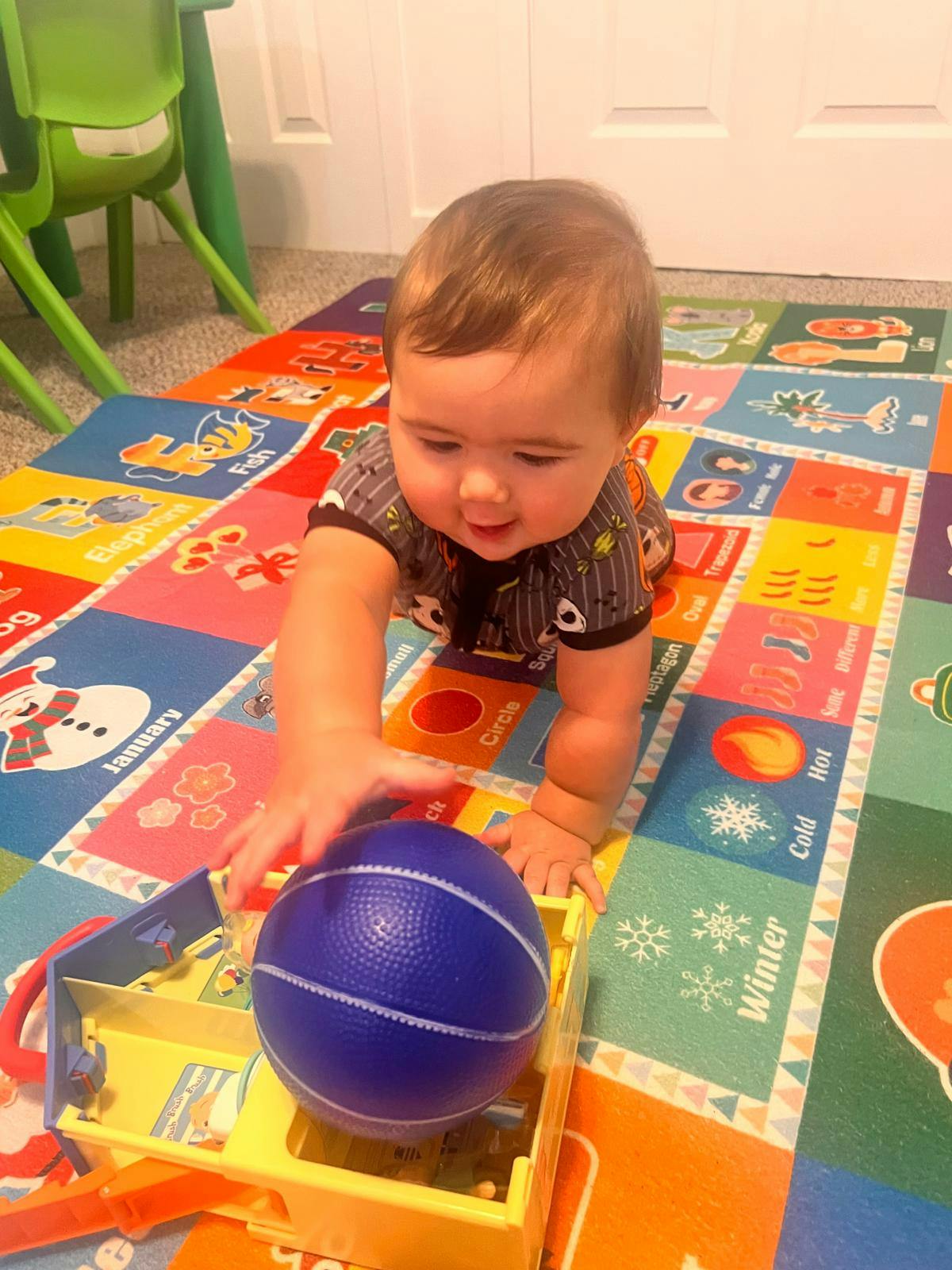 Child crawling on a colorful mat reaching for a blue ball