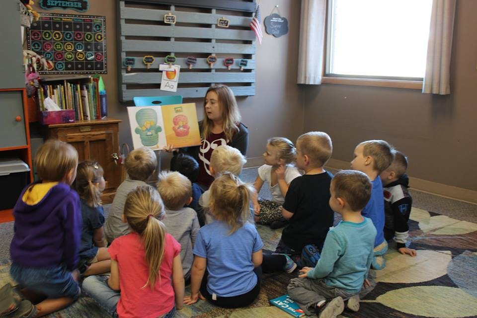 Adult reading a book to a group of children sitting on the floor
