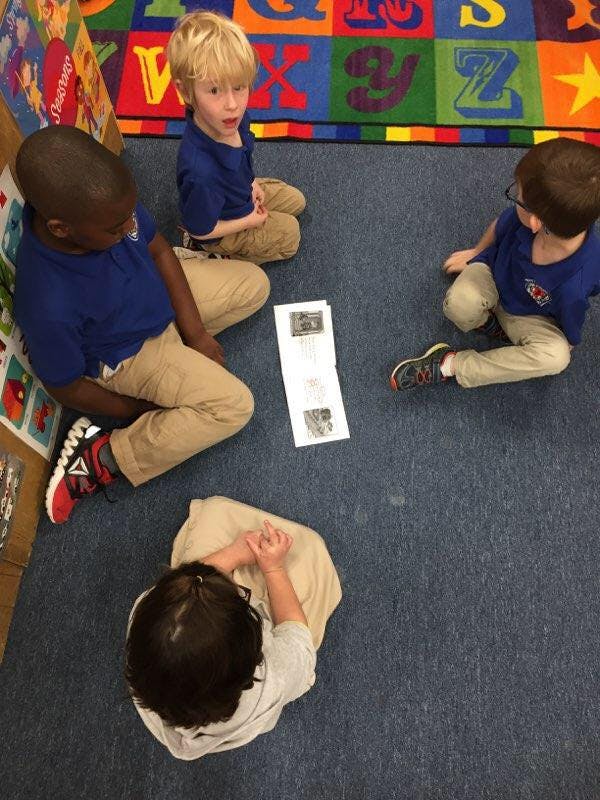 Four children sitting on a classroom floor around a piece of paper