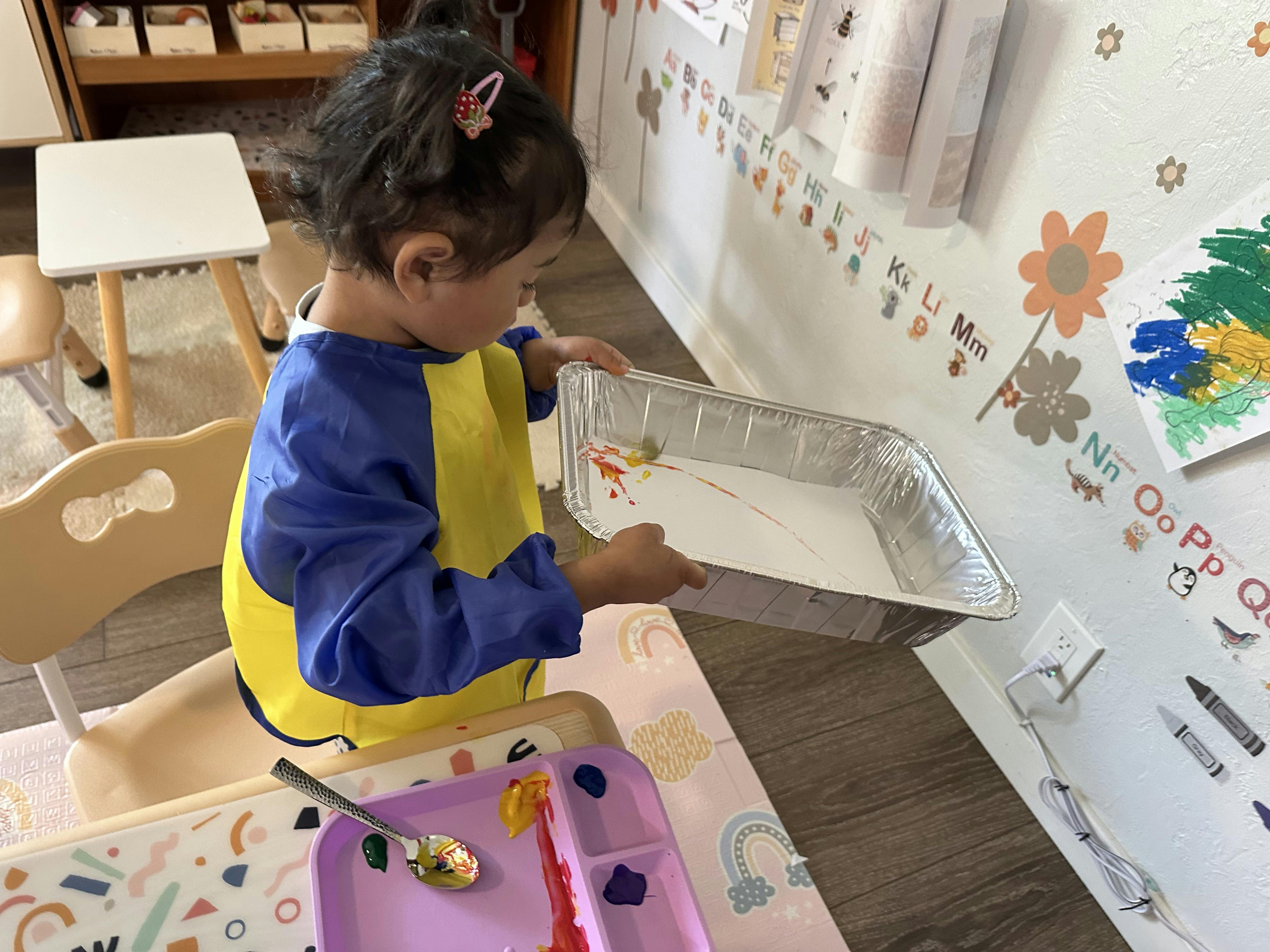 Child in smock holding a tray with sand