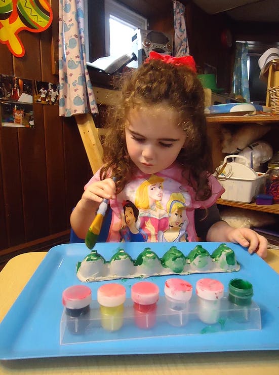 Child painting an egg carton with a brush