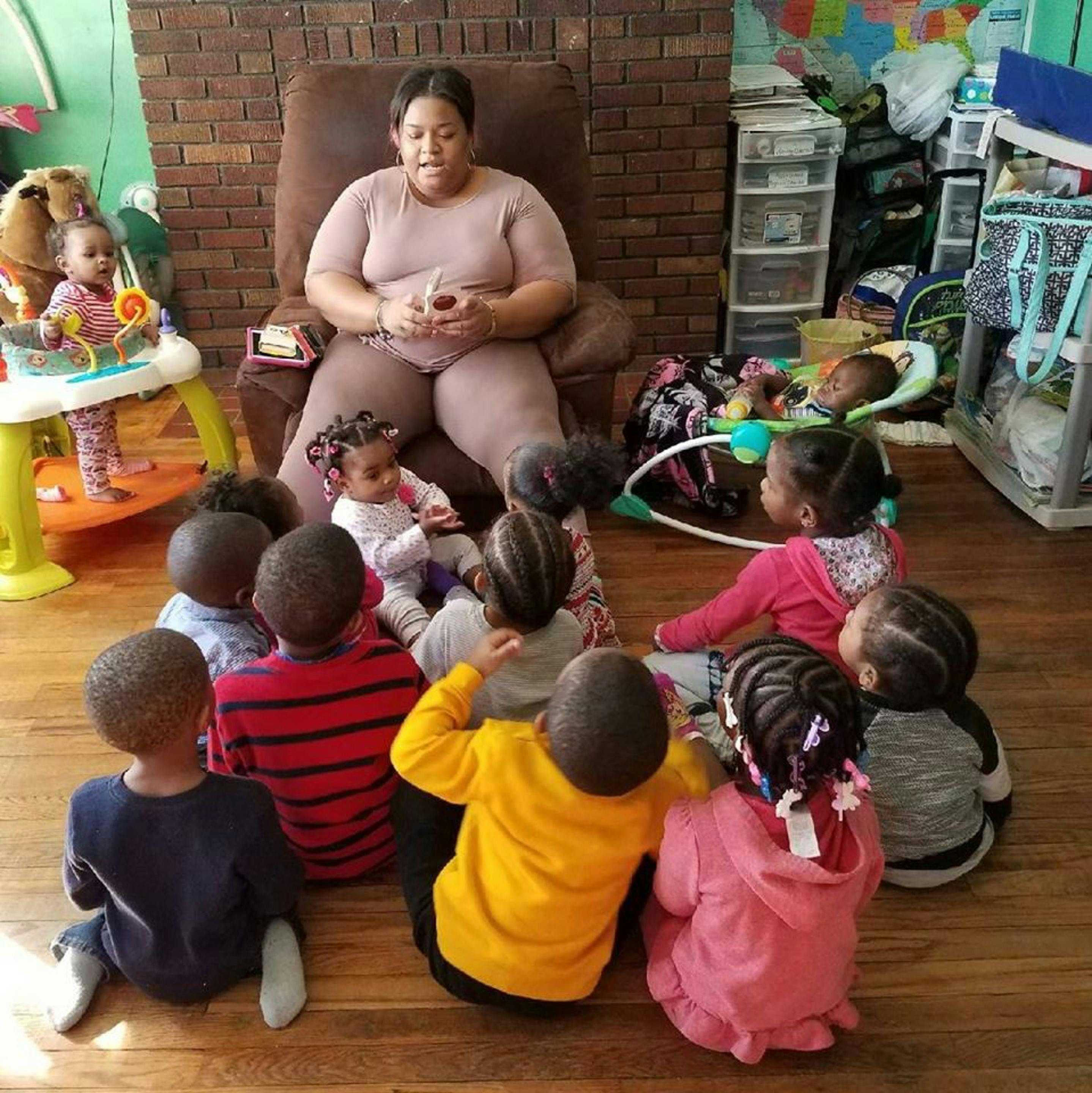 Person sitting in a chair with multiple children sitting on the floor around them