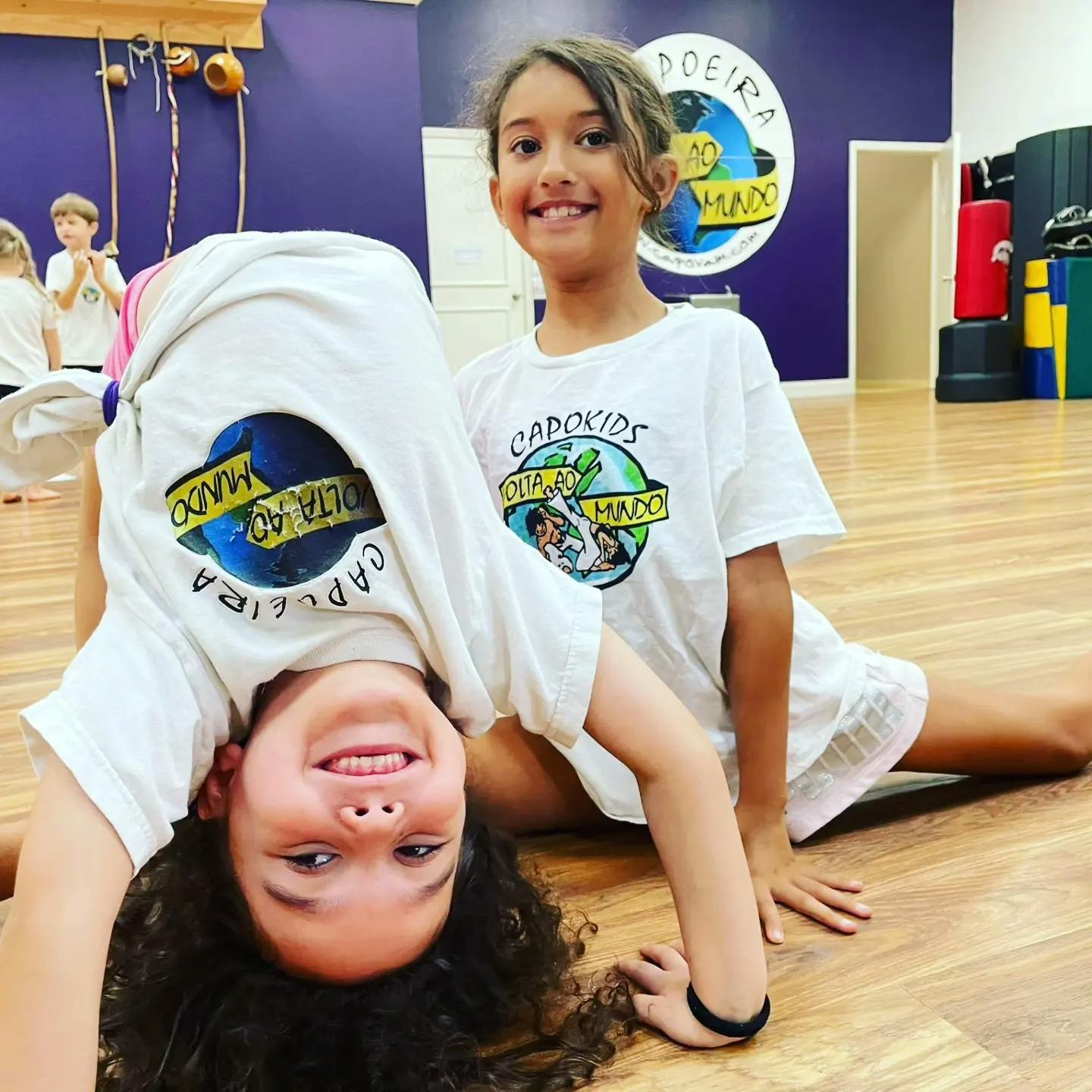 Two children in white shirts, one doing a handstand, the other sitting