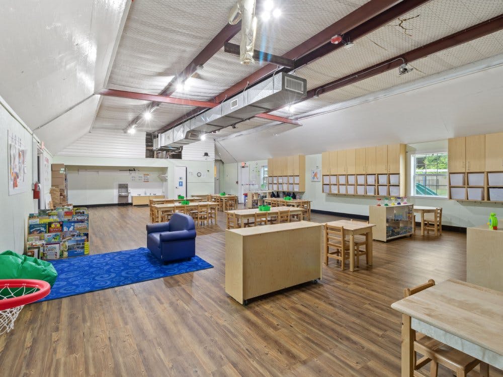 Empty children's classroom with small tables and chairs, a play rug, and storage