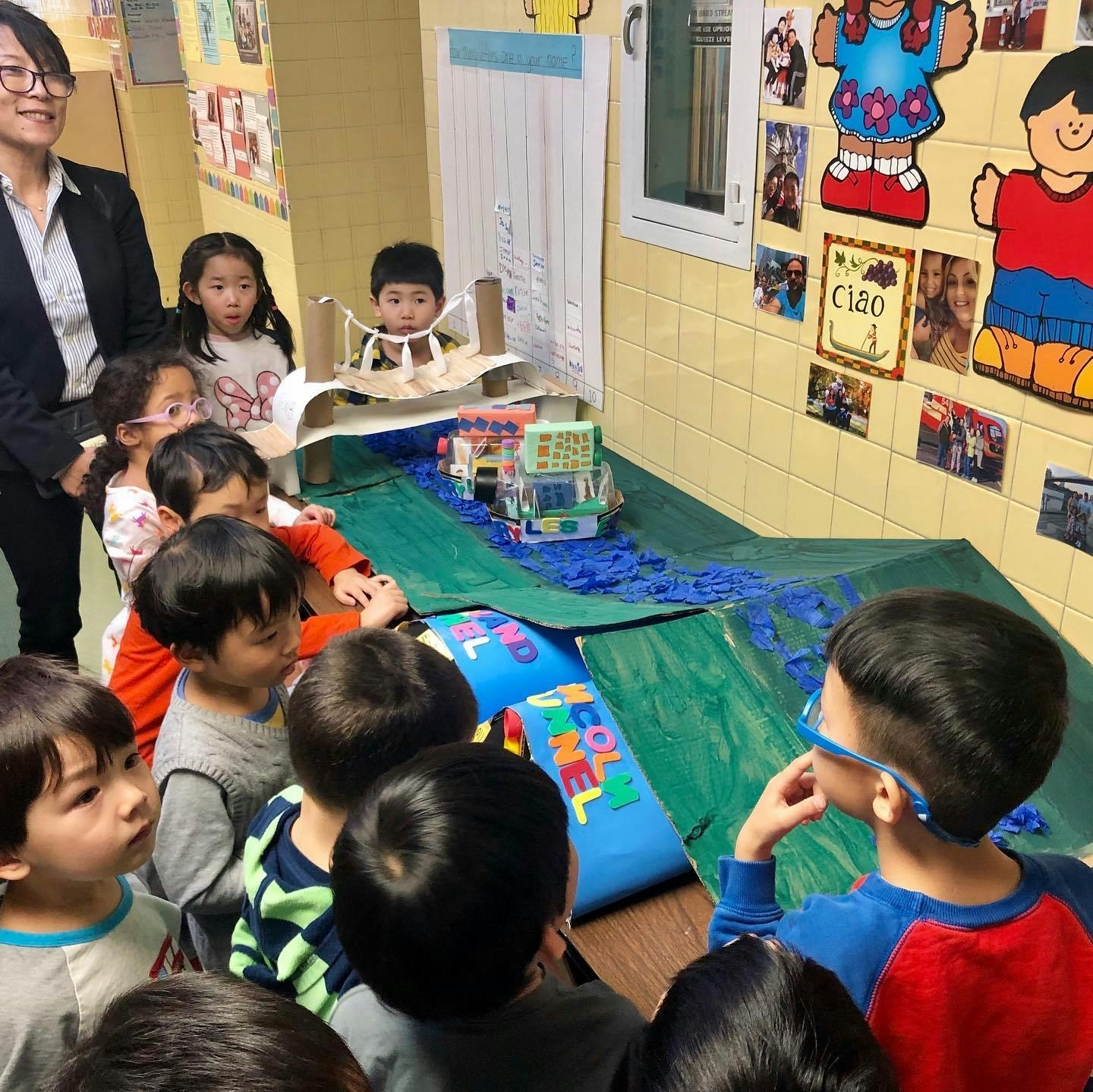 Children gathered around a toy bridge and river setup in a classroom