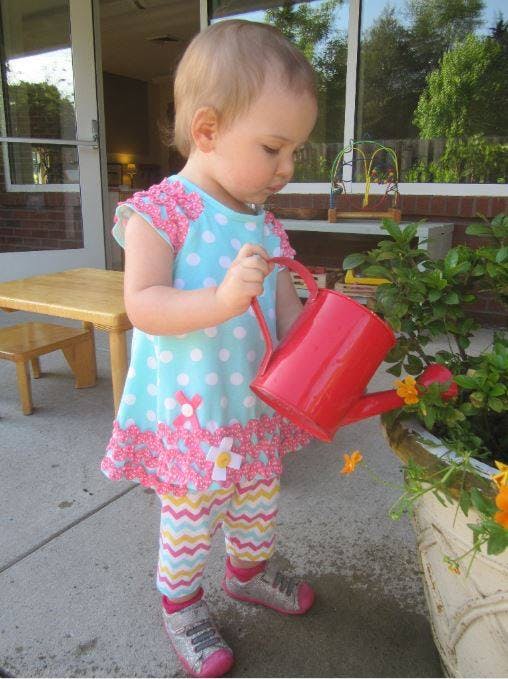Child watering a plant with a red watering can