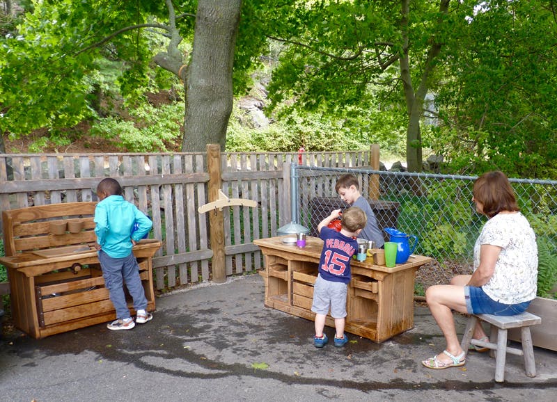 Three children and one adult playing outdoors with wooden furniture