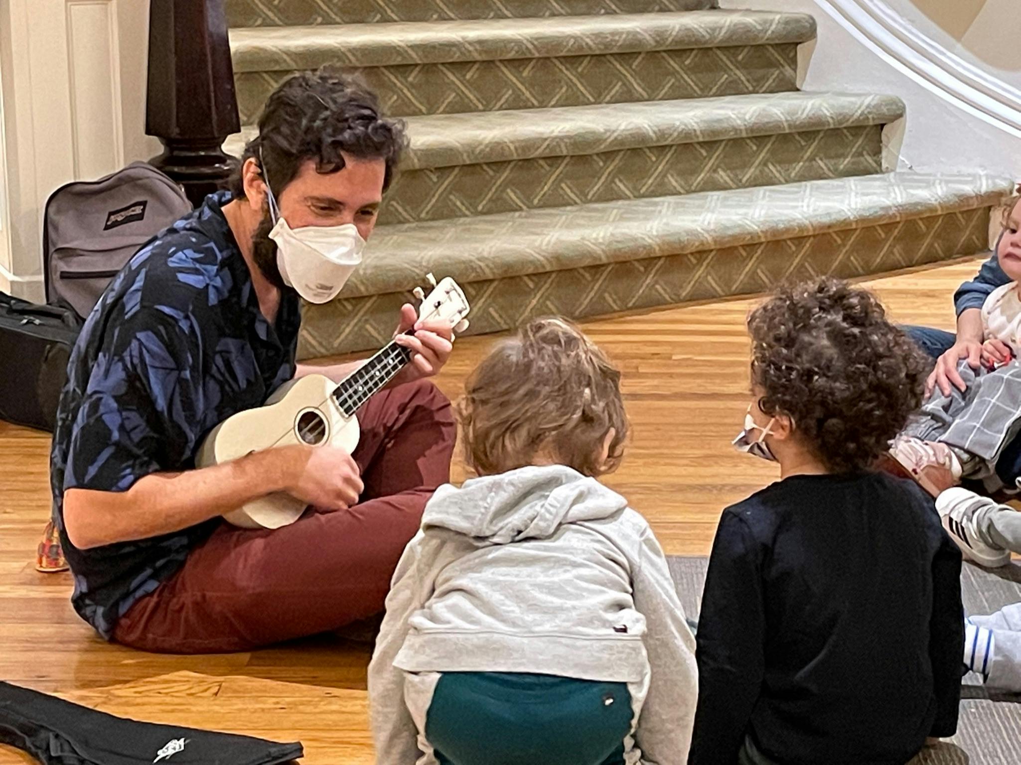 Person in mask playing ukulele for children