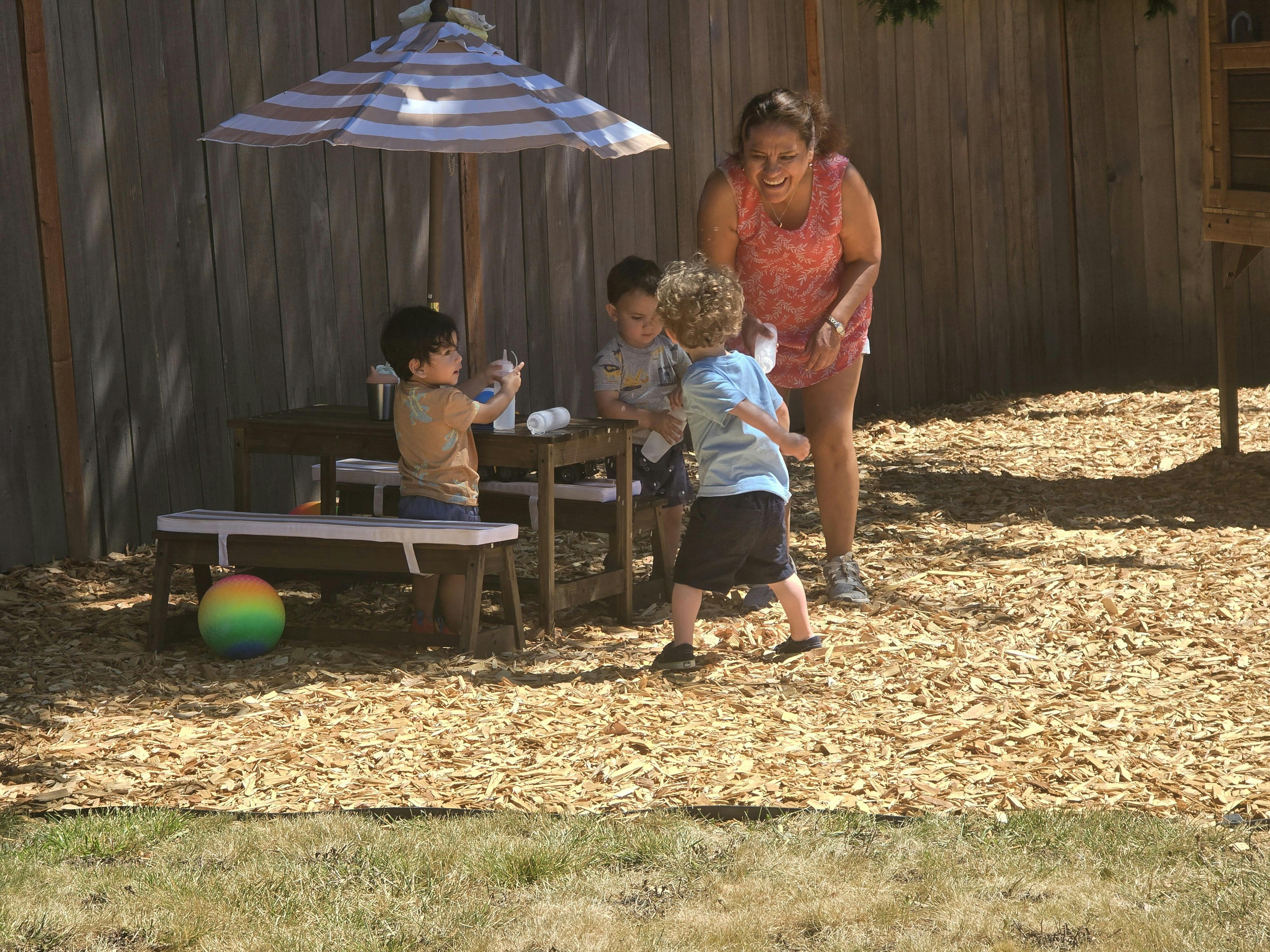 Adult and three children playing outdoors under an umbrella