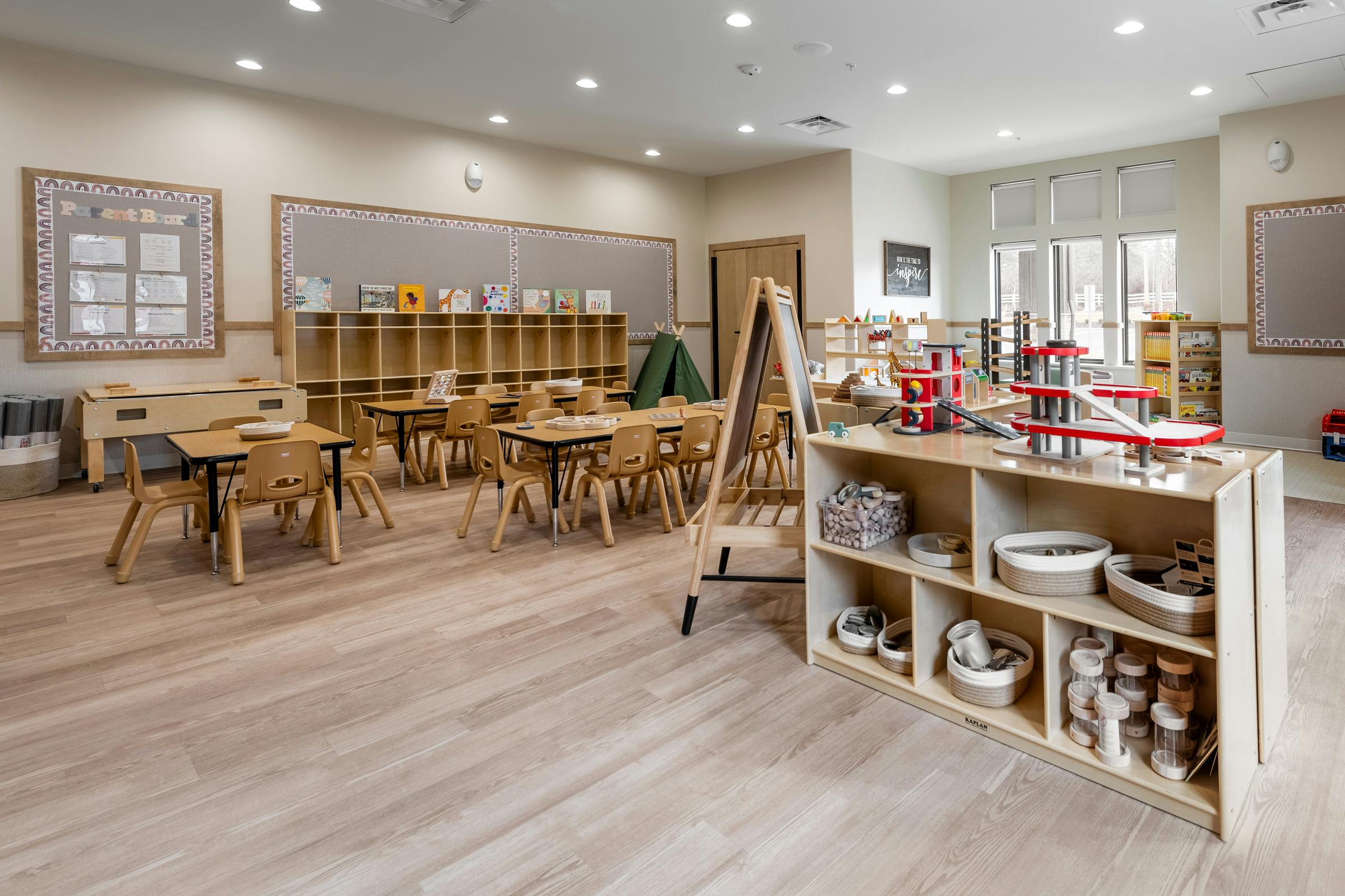 Classroom with small tables and chairs, shelves with learning materials