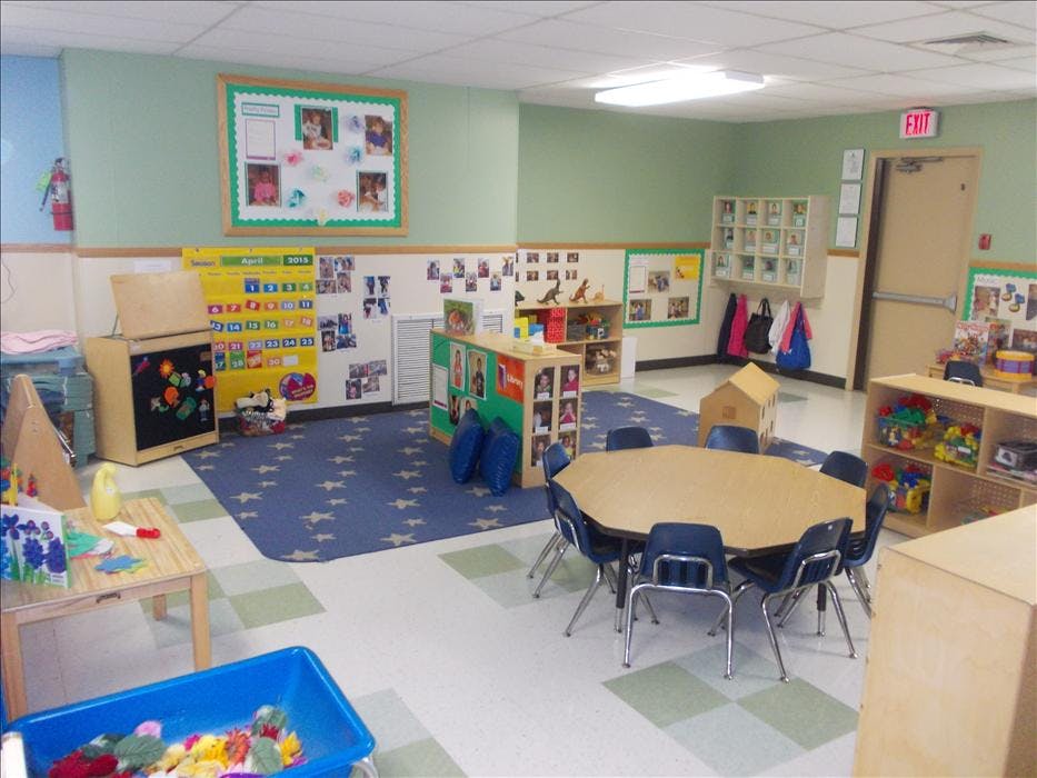 Classroom with a table and chairs, shelves of toys, and a calendar on the wall