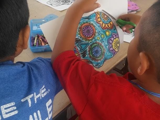 Two children at a table, one cutting out a colorful drawing