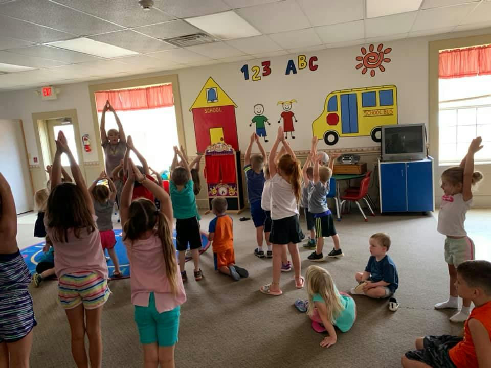 Children in a classroom doing yoga poses with arms raised