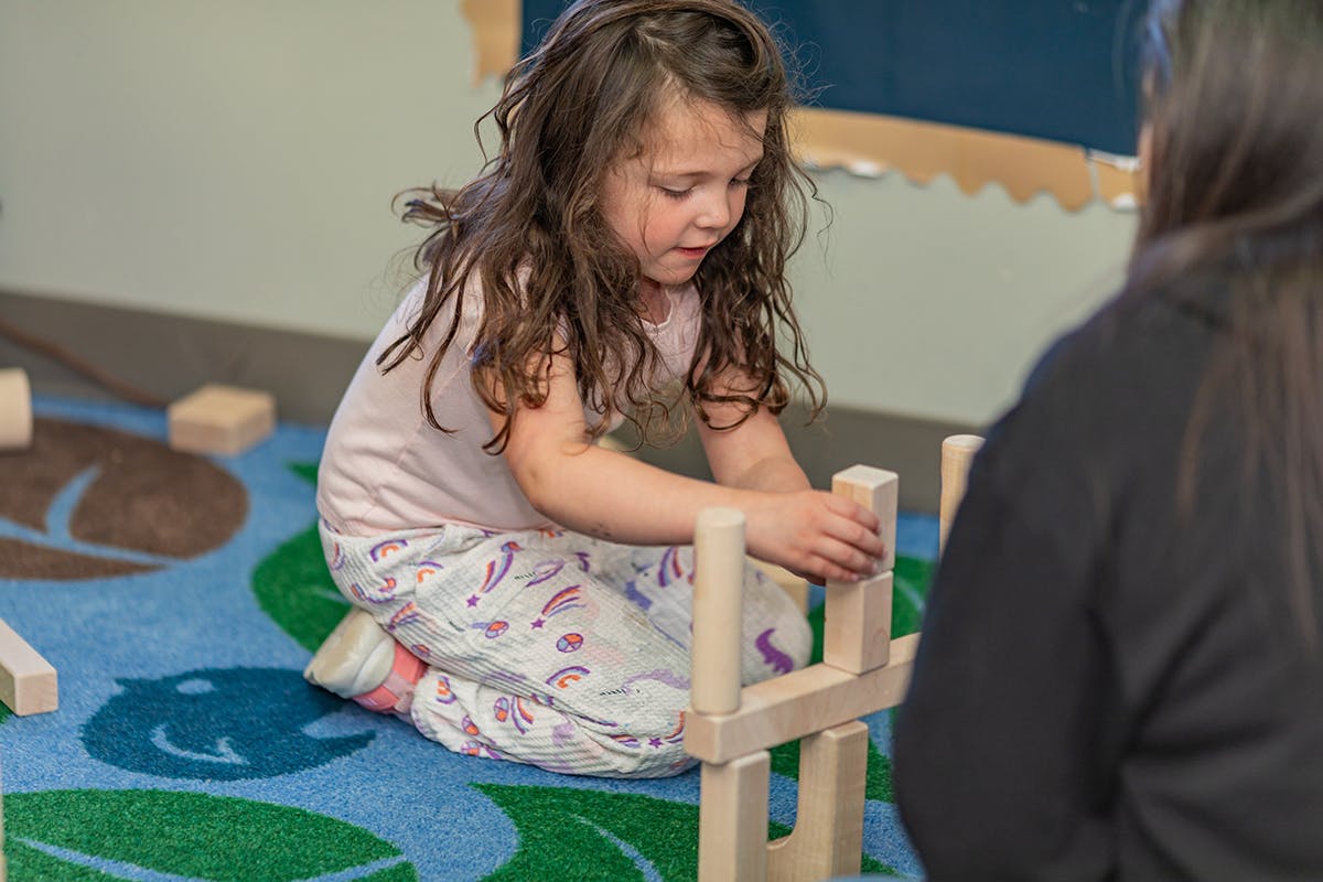 Child kneeling on a rug, building with wooden blocks