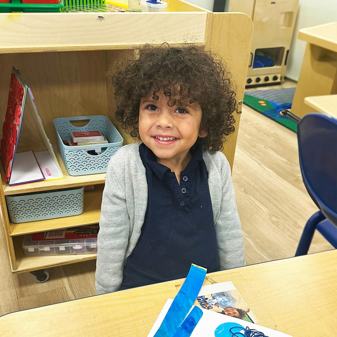 Child with curly hair smiling in a classroom