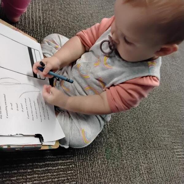Child on floor holding a crayon over a book