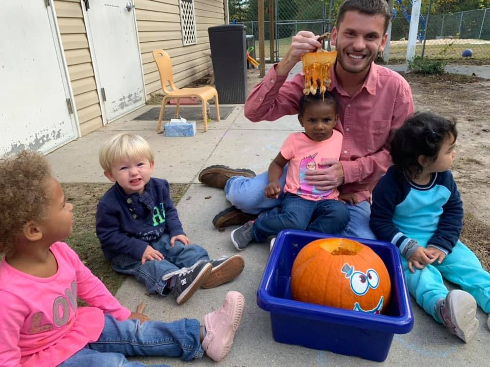 Adult and children sitting on the ground with a pumpkin