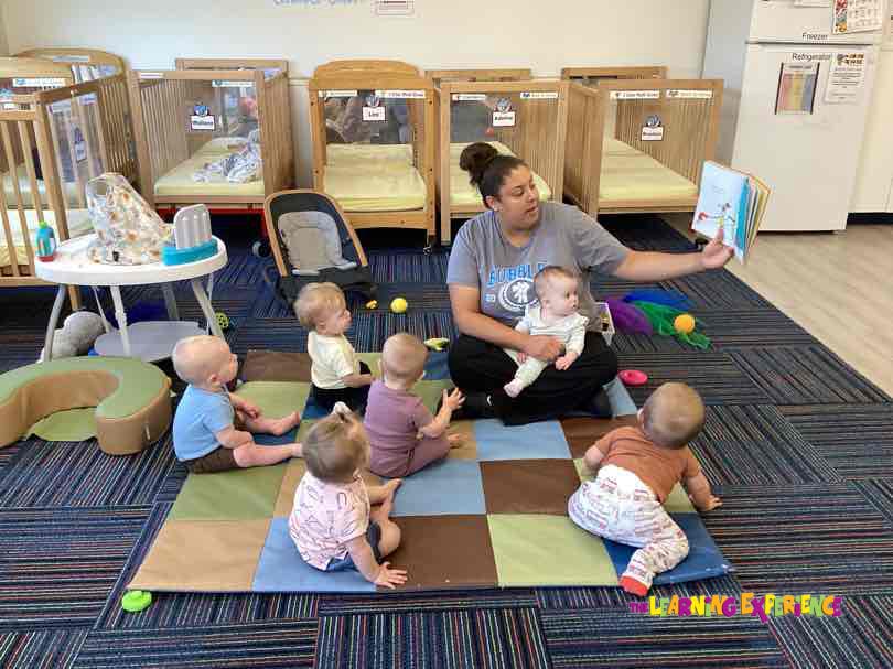 Person holding a child and reading a book to a group of children
