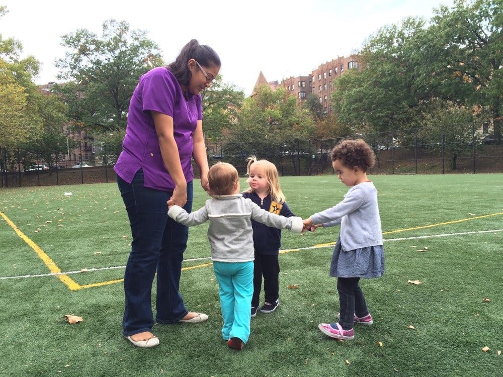 Person and three children holding hands in a circle on a field