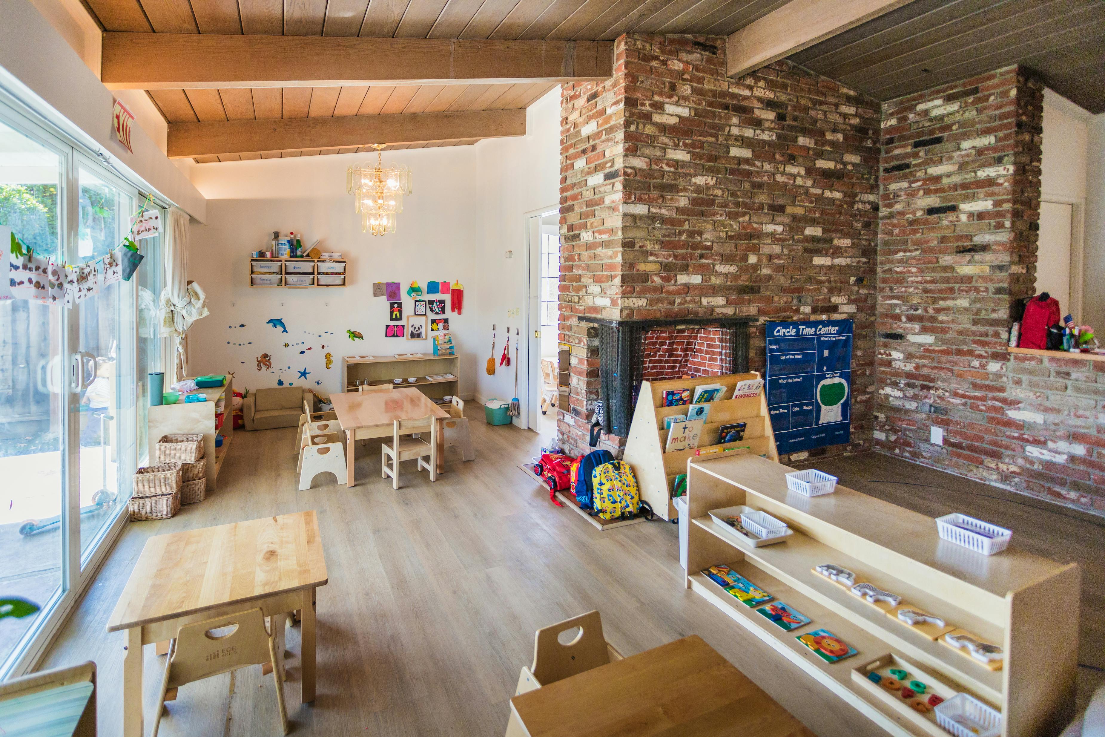 Classroom with small wooden tables and chairs, shelves with learning materials