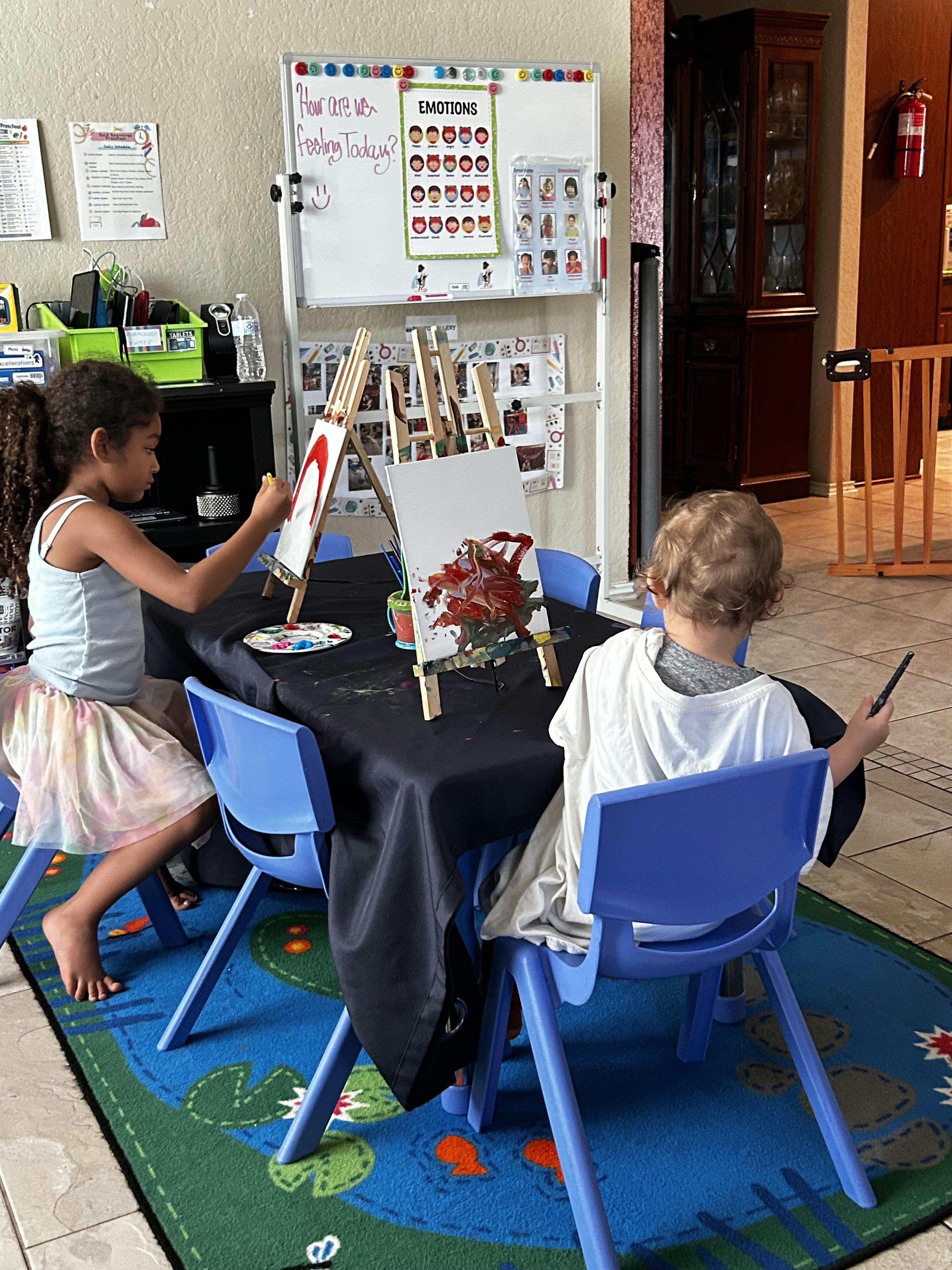 Two children painting on small easels at a table