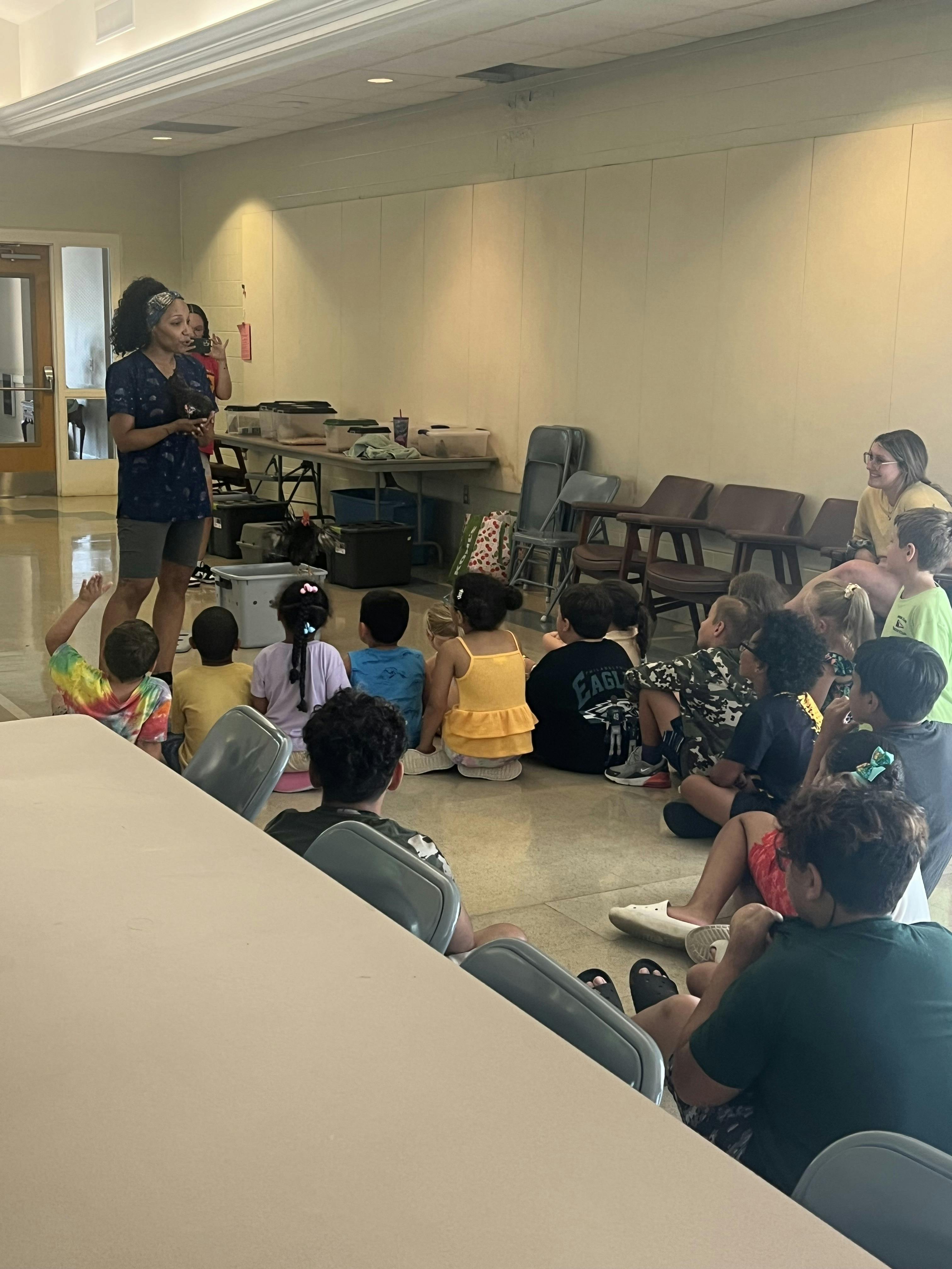 Person standing and speaking to a group of children sitting on the floor