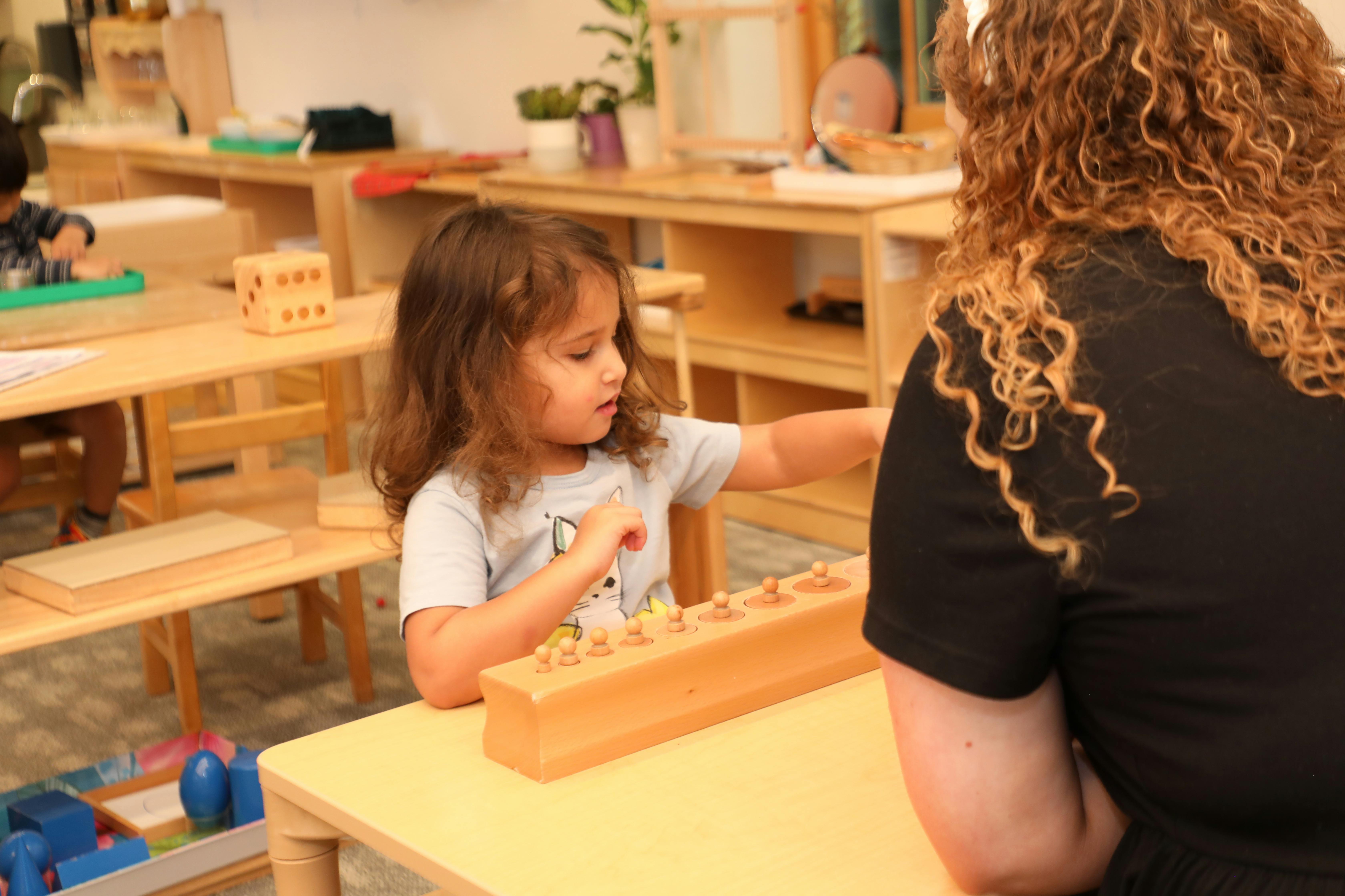 Child playing with a wooden toy at a table with an adult