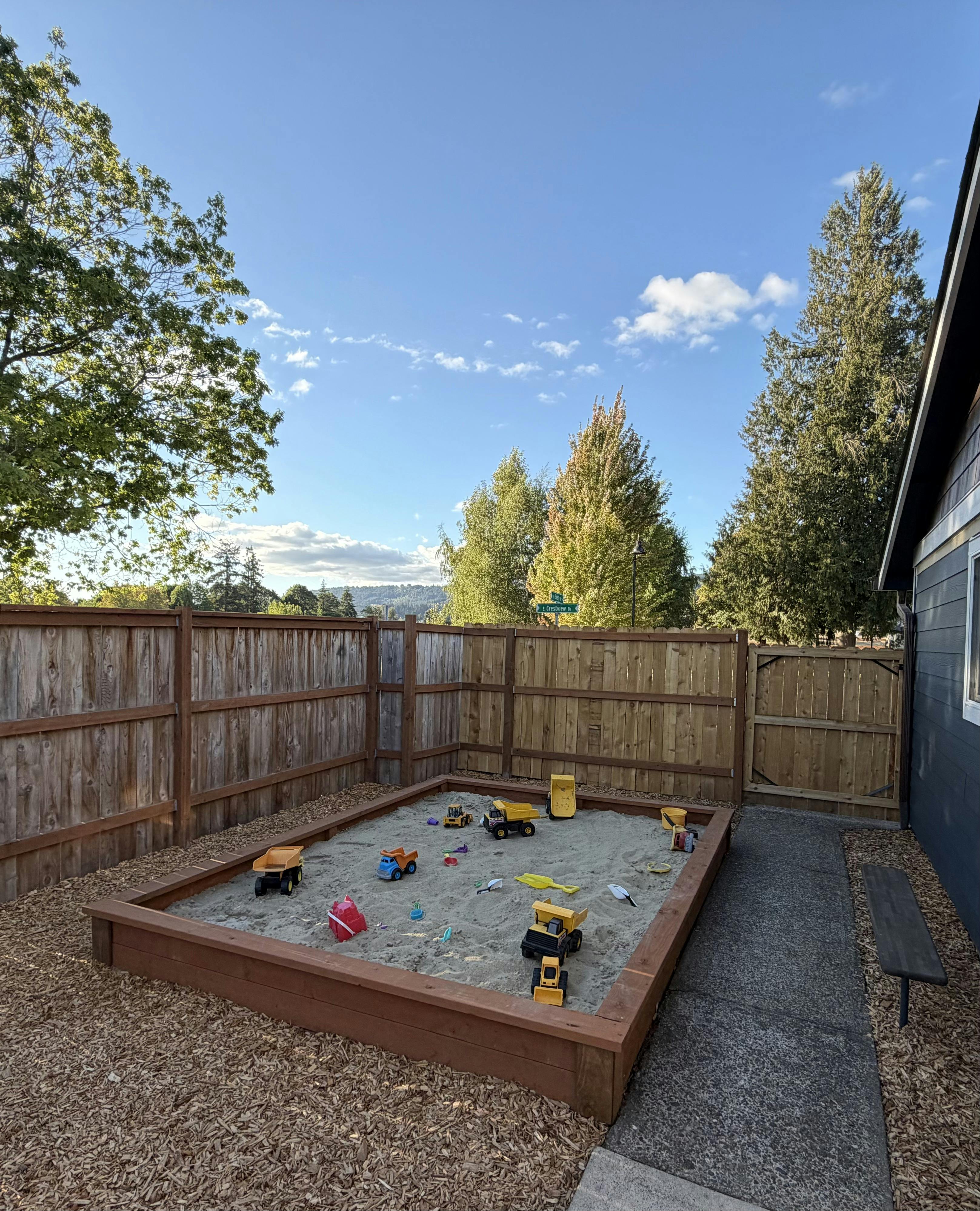 Sandbox with toy construction trucks in a residential backyard
