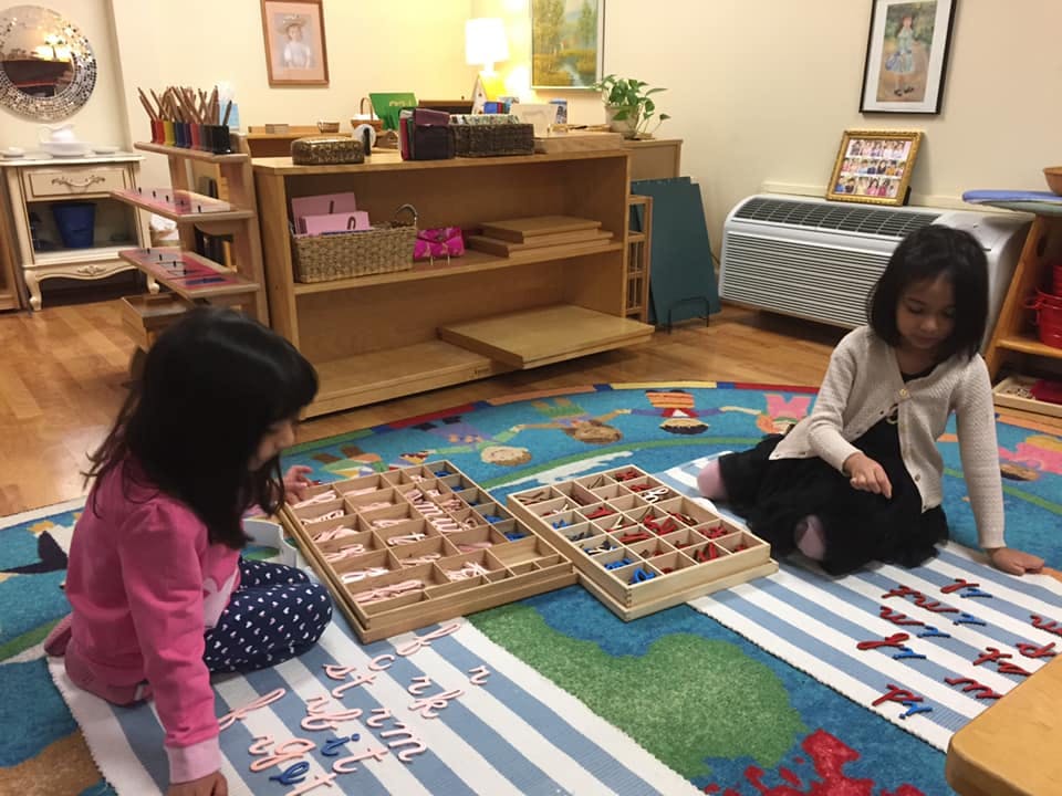 Two children playing with wooden blocks and letters on a rug in a classroom