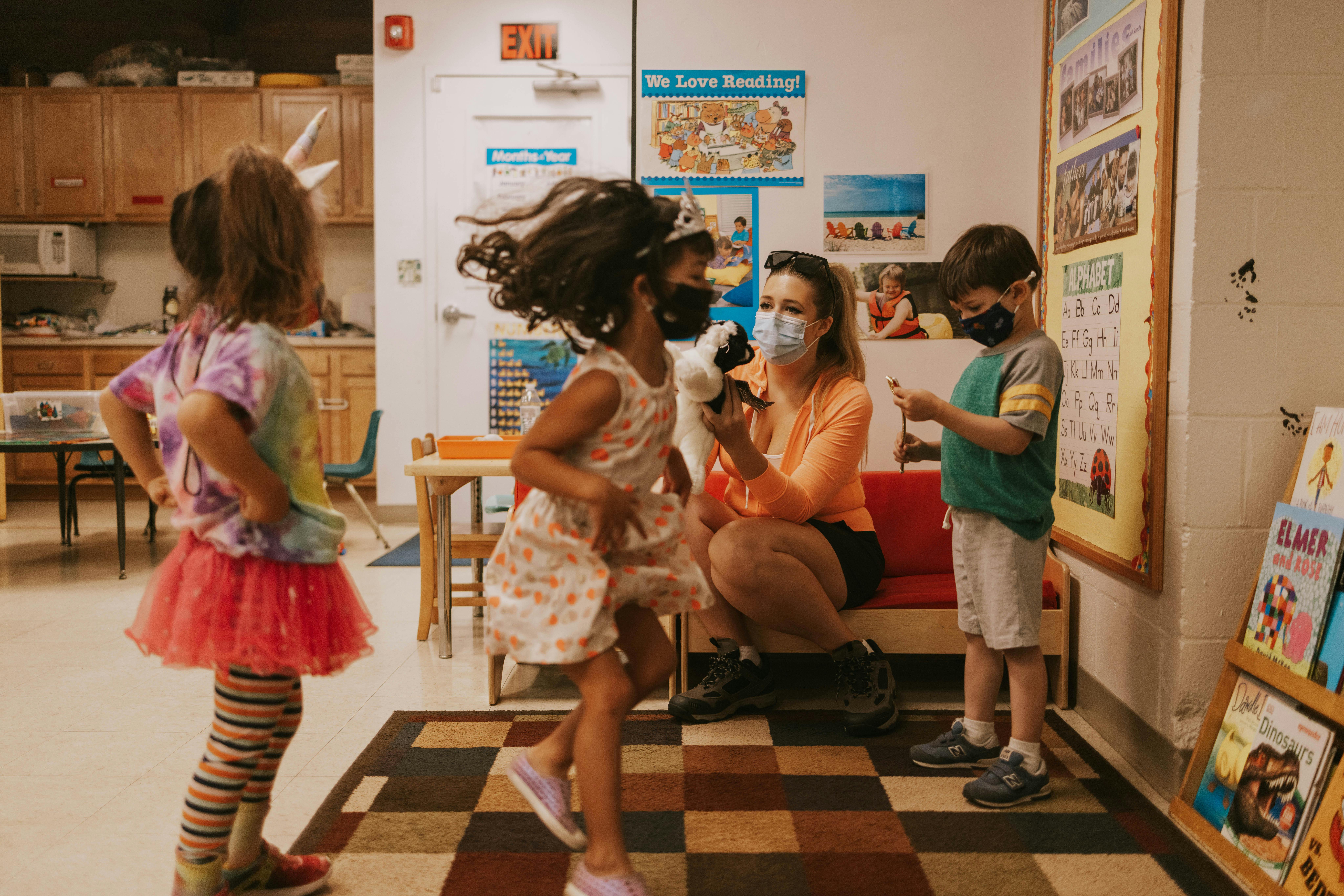 Children and an adult in masks interacting in a classroom