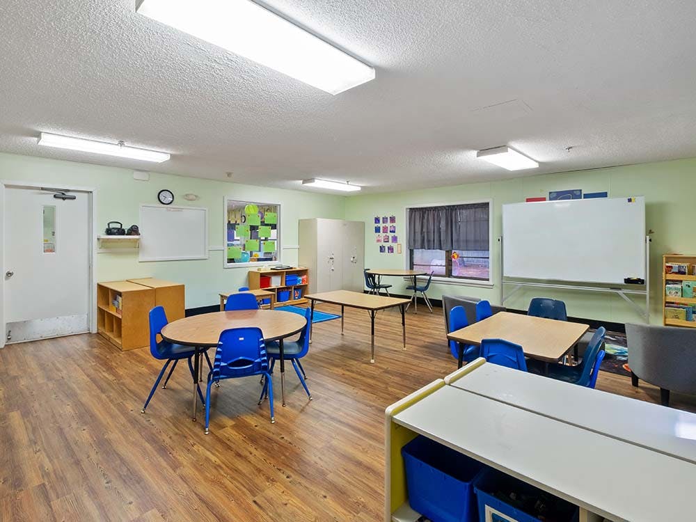 An empty classroom with small tables and chairs, whiteboards, and cubbies