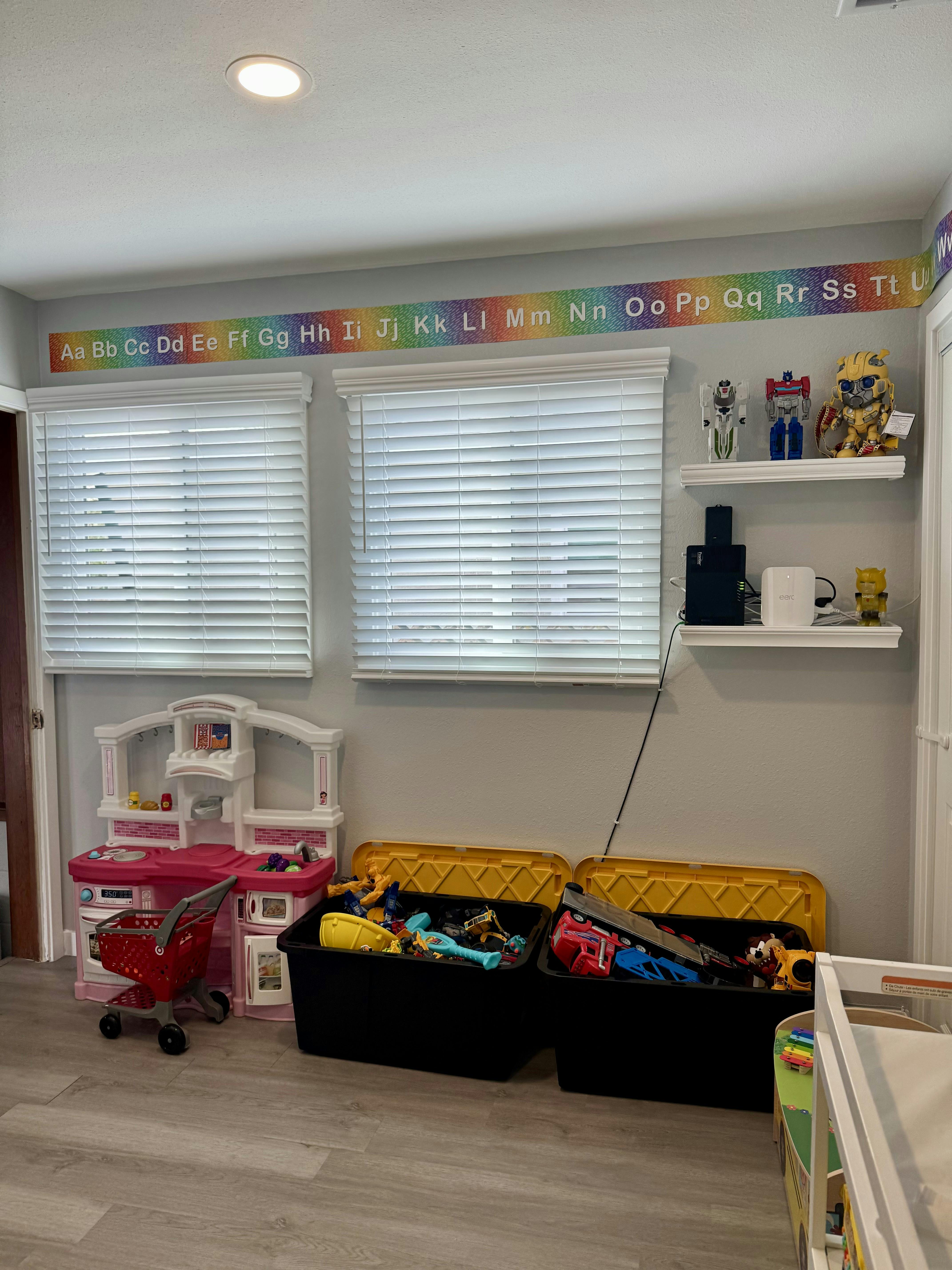 Play kitchen and shopping cart next to two toy bins with a rainbow alphabet border above