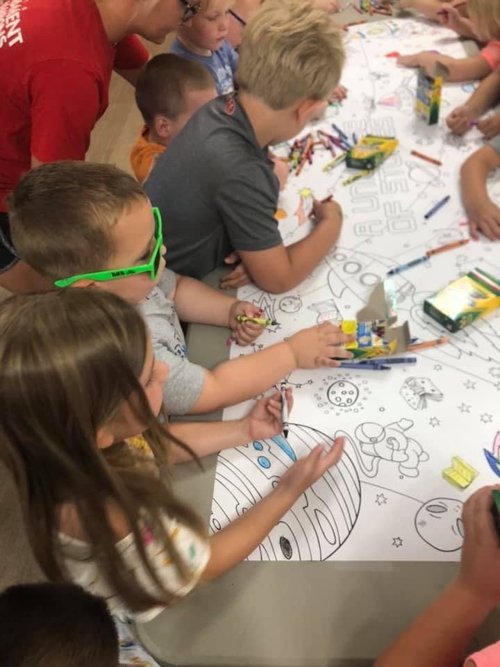 Children coloring a large space-themed drawing on a table