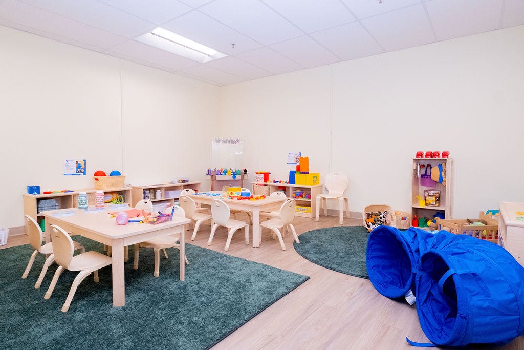 Classroom with small tables and chairs, shelves with toys, and a blue play tunnel