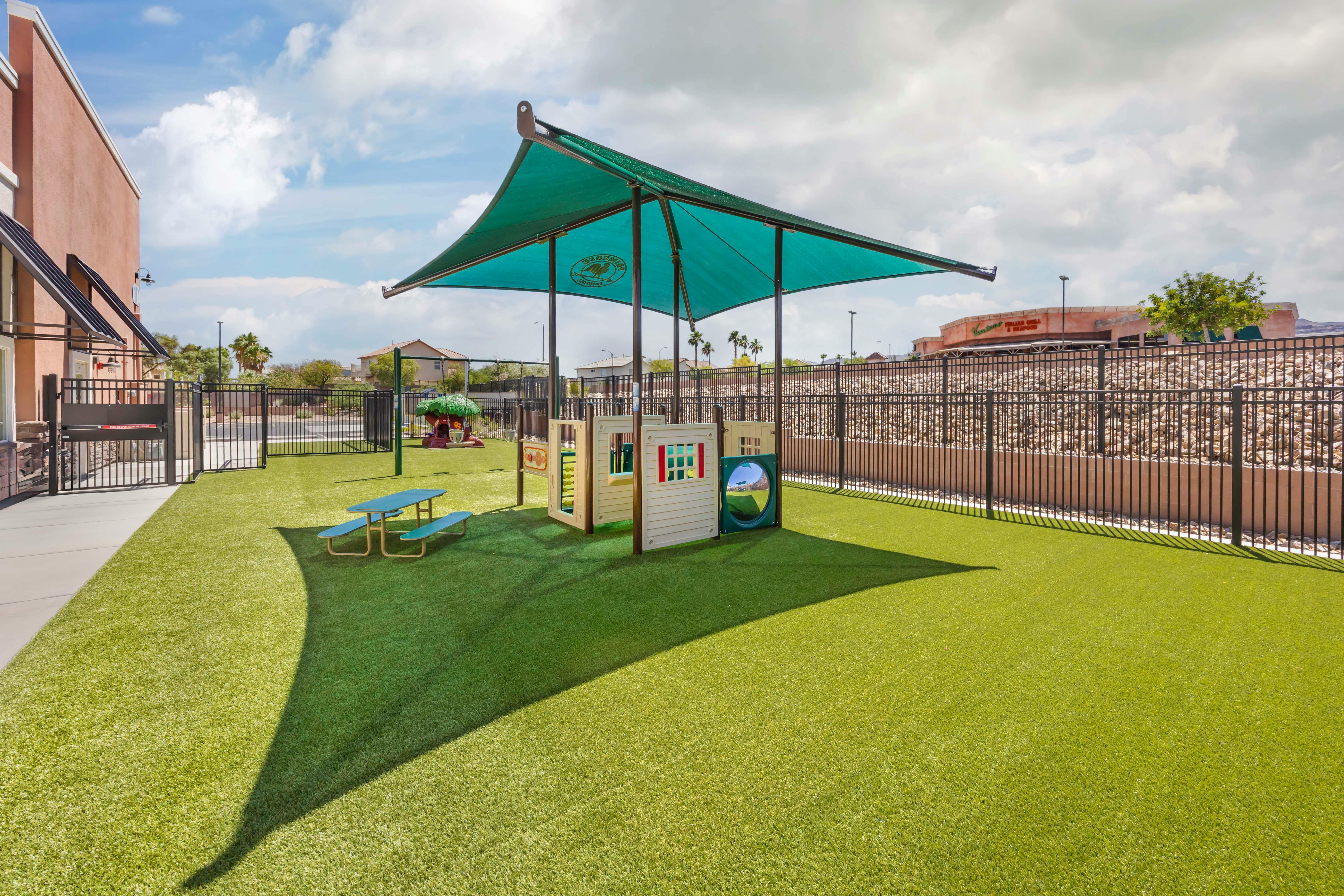 Outdoor playground with artificial turf, covered by a green canopy