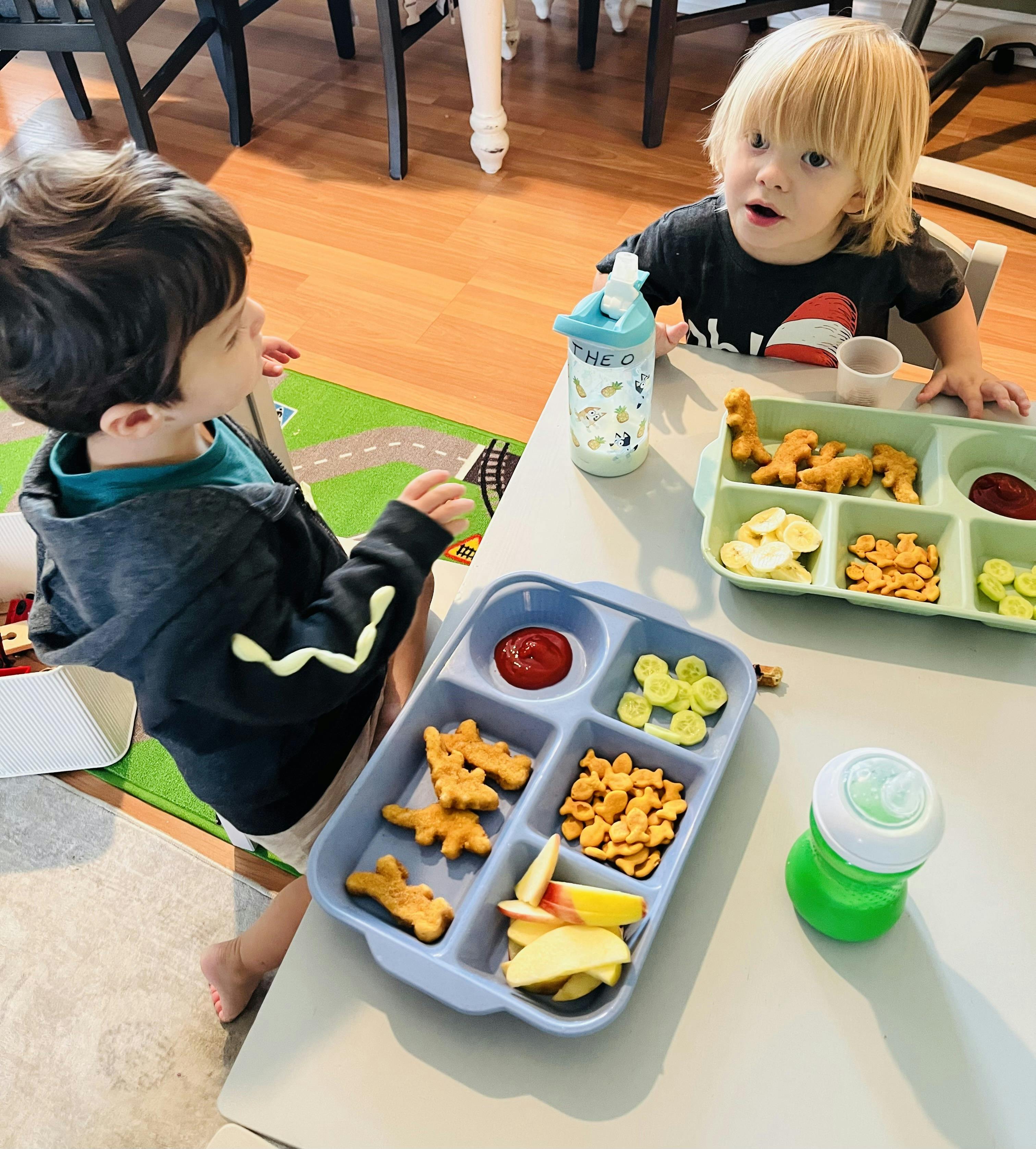Two children sitting at a table with divided plates of food