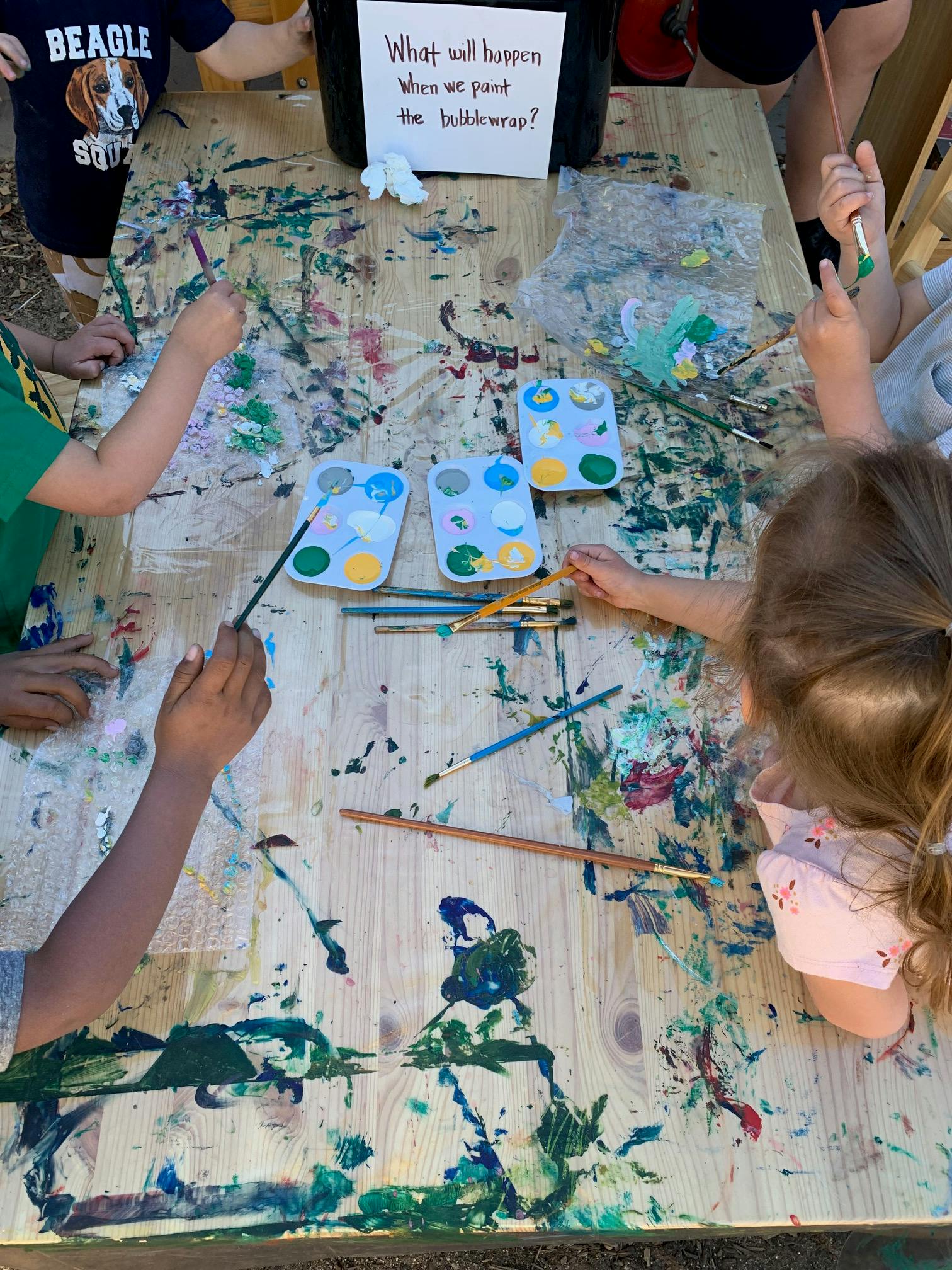 Children painting at a table with paint palettes and brushes