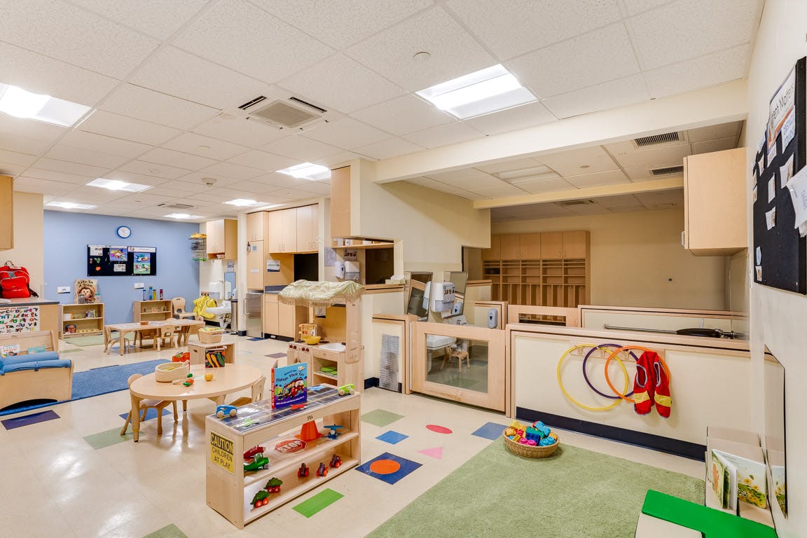 Empty classroom with small tables, chairs, and shelves with toys and learning materials