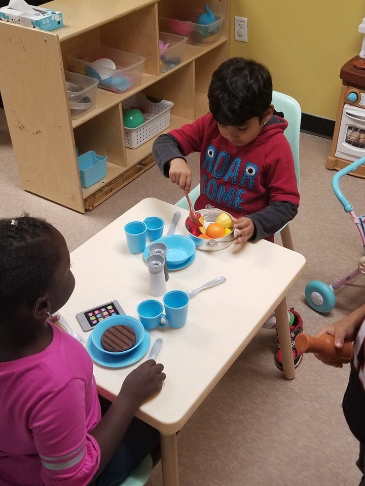 Child playing with toy food at a table with another child