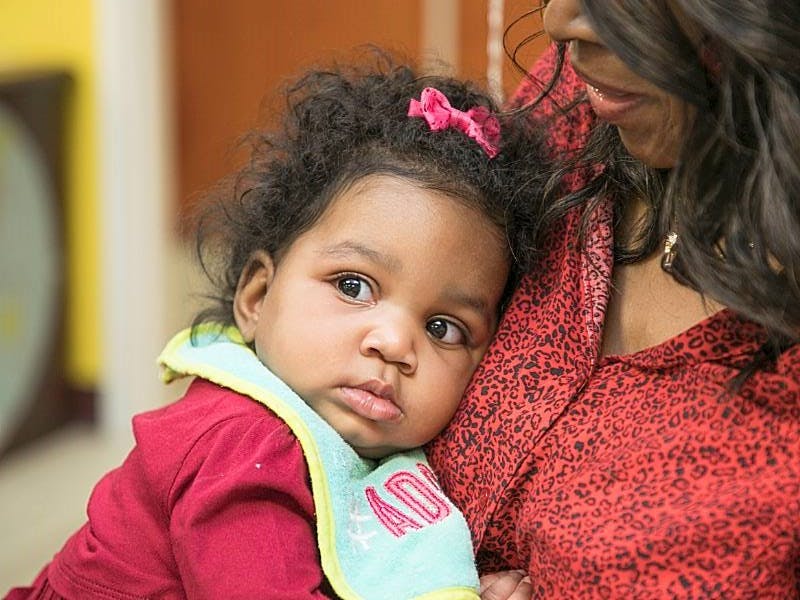 Child with a pink bow in hair resting head on a person's shoulder