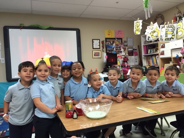 Group of children in a classroom gathered around a table with a bowl