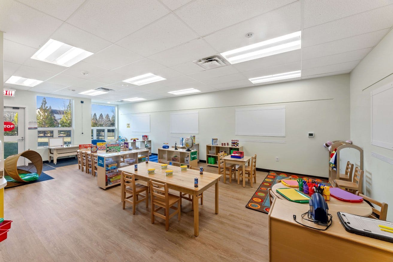 Empty children's classroom with small tables, chairs, and shelves of toys
