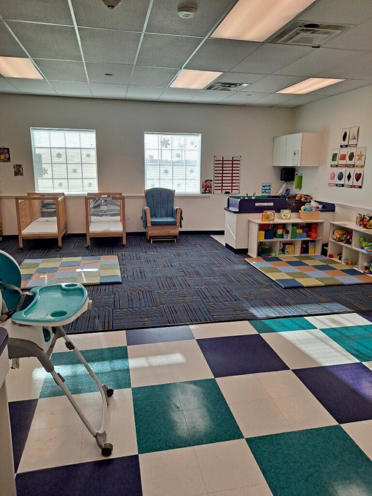 Empty classroom with cribs, a rocking chair, and play areas