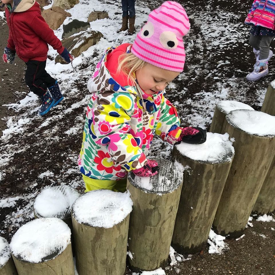 Child in winter clothing touching snow on wooden posts