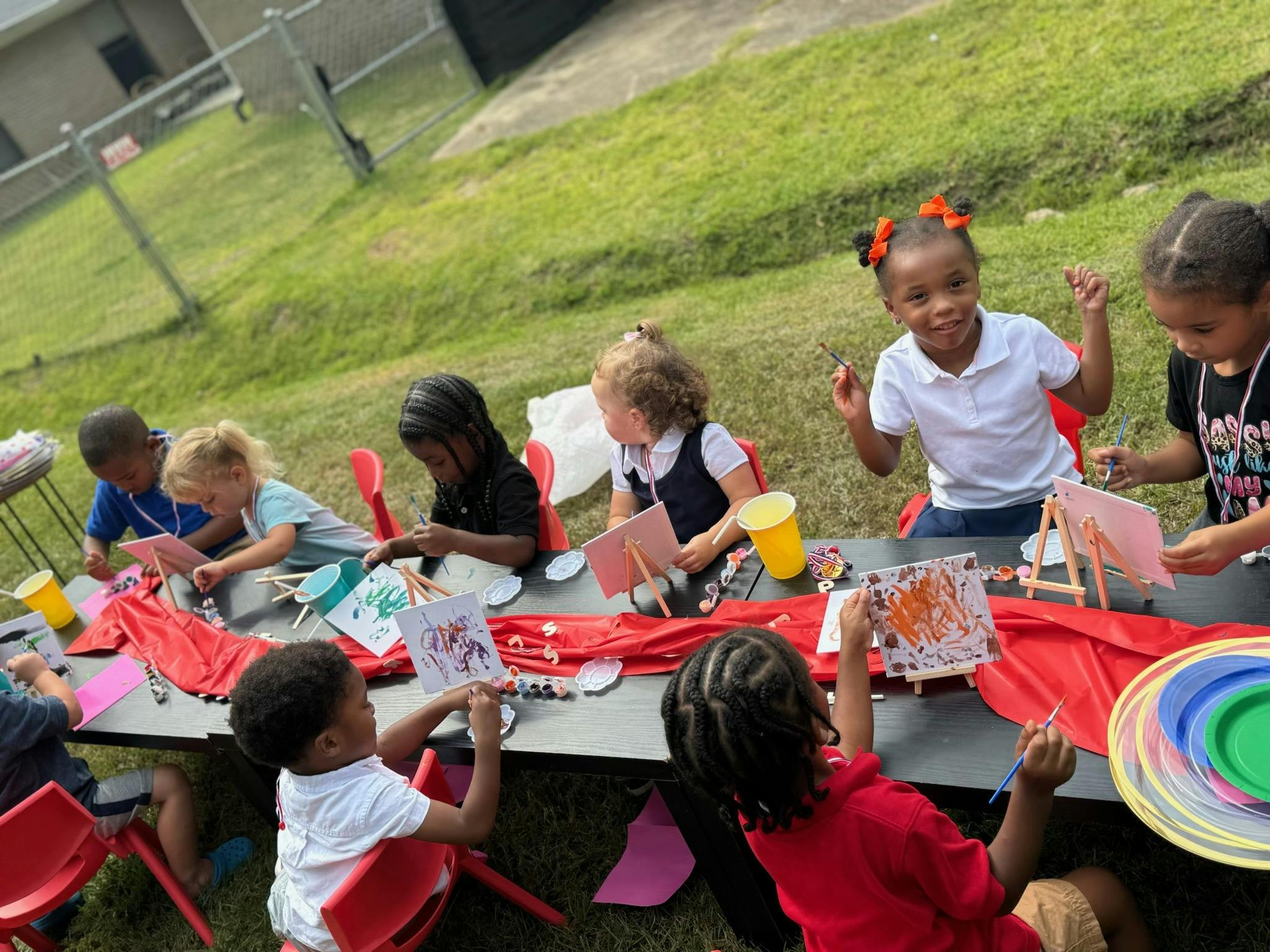Children painting at a long black table outdoors