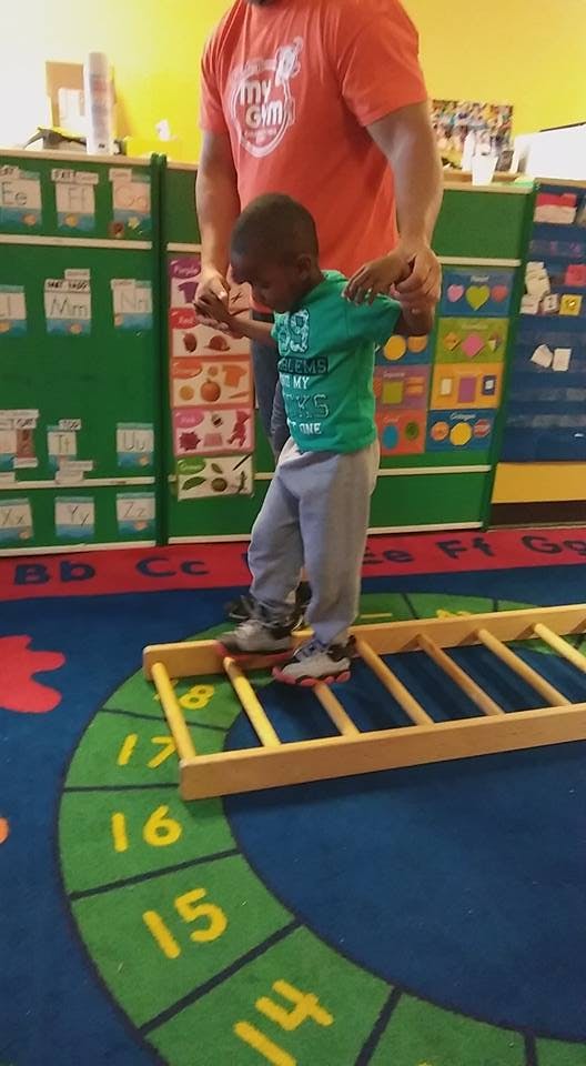 Adult helping a child walk on a wooden ladder on the floor