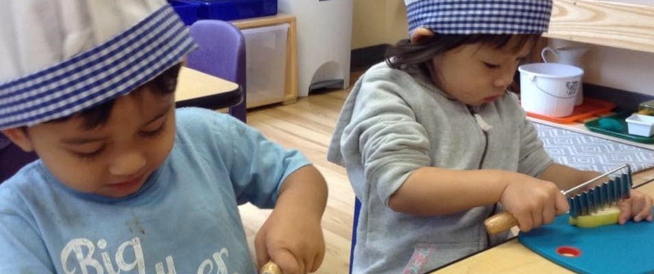 Two children in a classroom, one using a grater