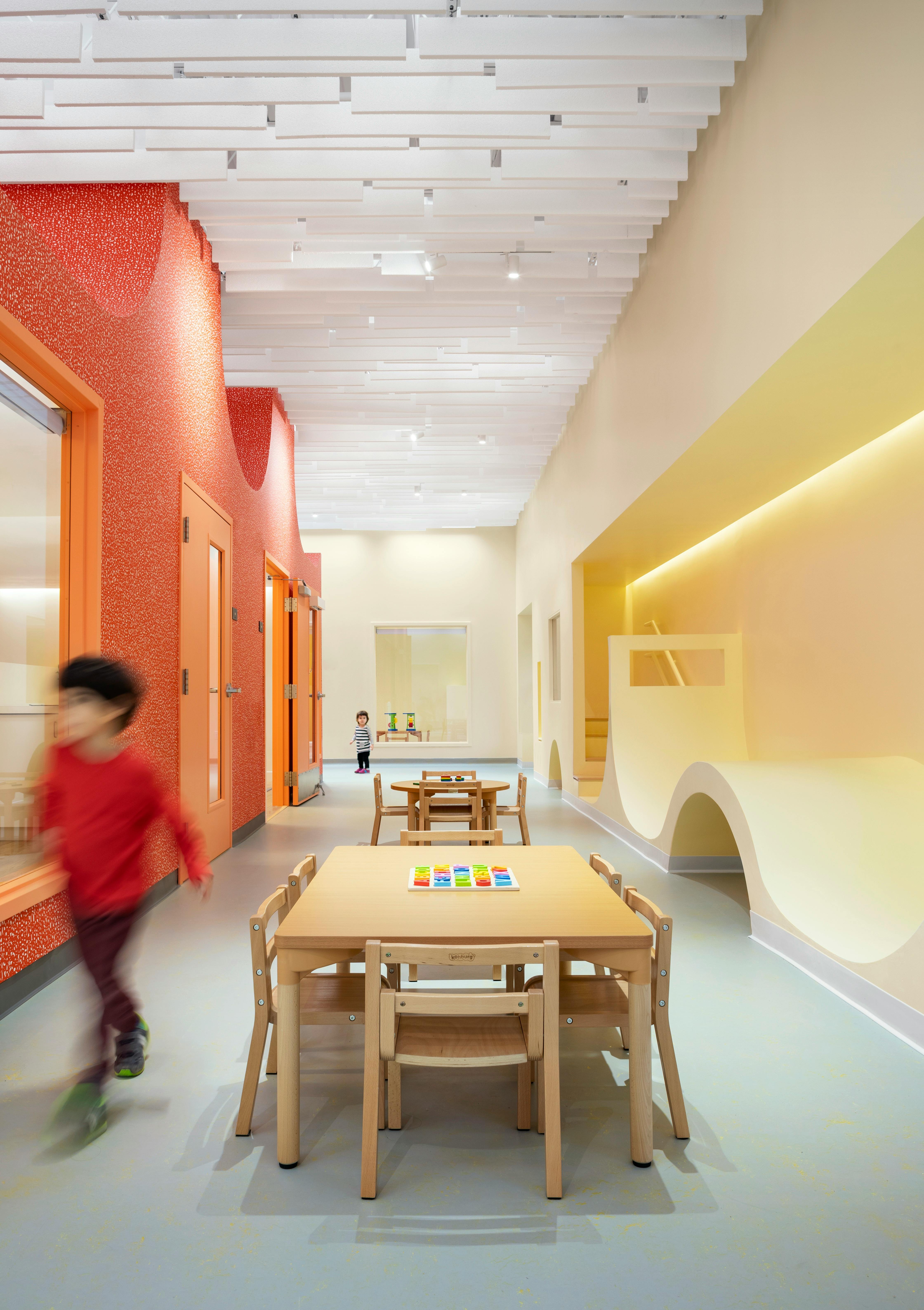 Child running in a brightly lit hallway with small tables and chairs