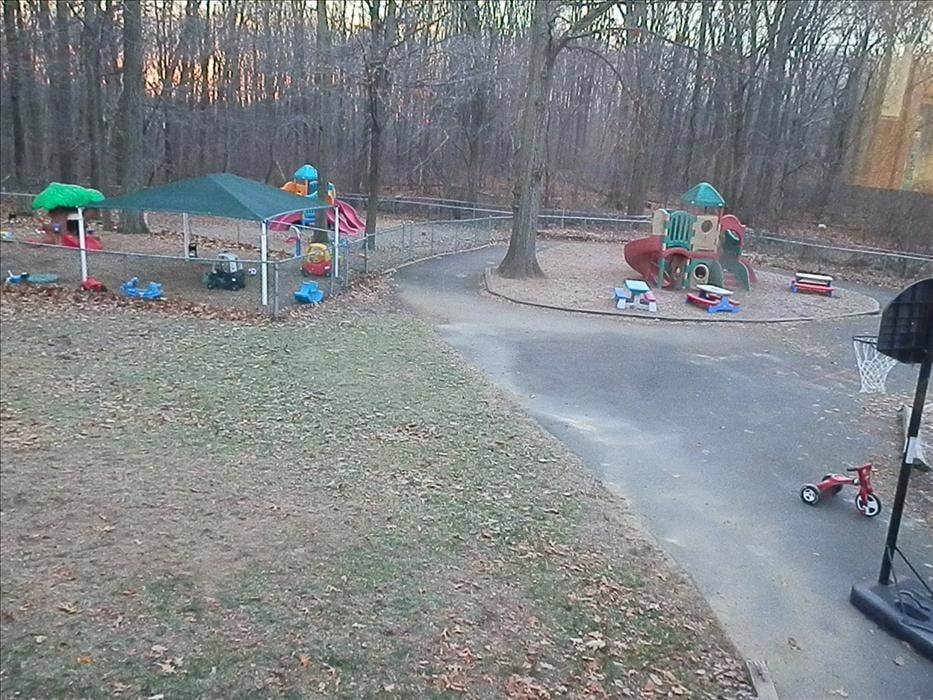 Outdoor playground with fenced areas, play structures, and a basketball hoop