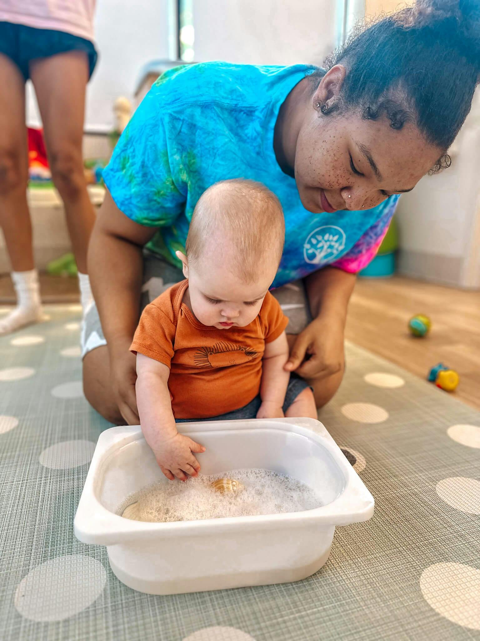 Person kneeling with a child playing in a bin of rice